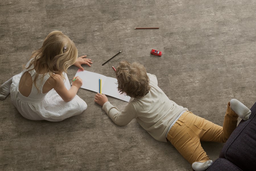 Two children drawing on paper while laying on carpet